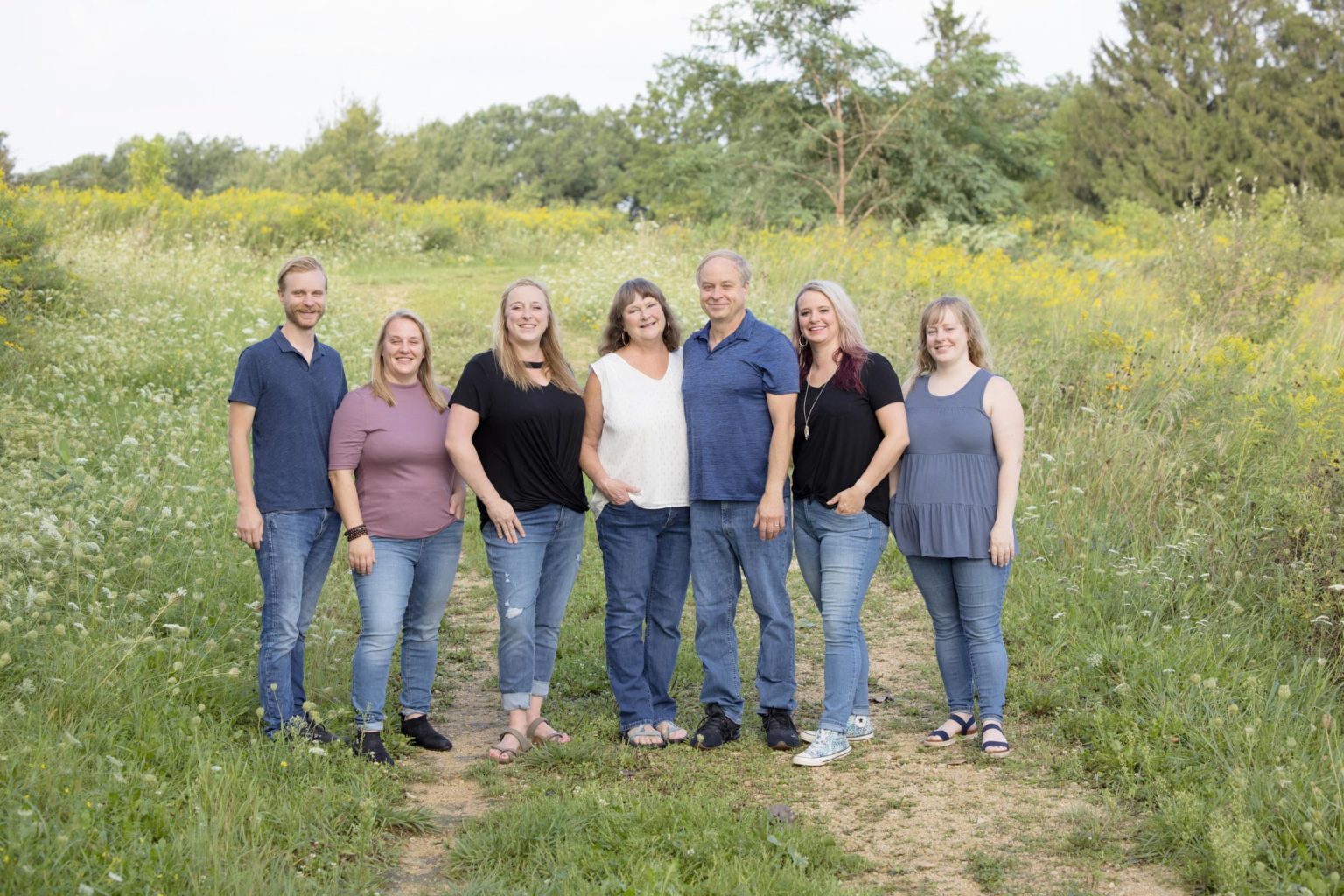 Extended family stands together on a nature trail surrounded by wildflowers and greenery during an outdoor portrait session with Mueller Photography in La Crosse, WI.