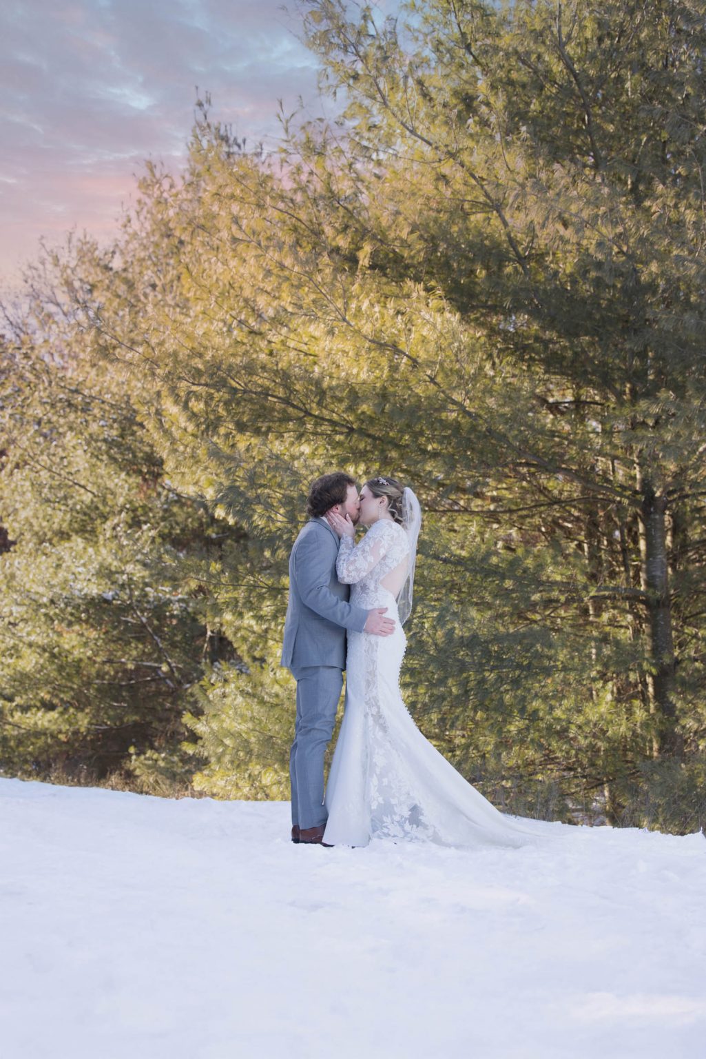Bride and groom share a winter kiss in the snow with golden pines behind them near The Florian Gardens in Eau Claire, WI, captured by Mueller Photography