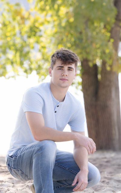 High school senior poses on a sandy riverside path in jeans and a light blue shirt during a natural, outdoor senior portrait session with Mueller Photography in La Crosse, WI.