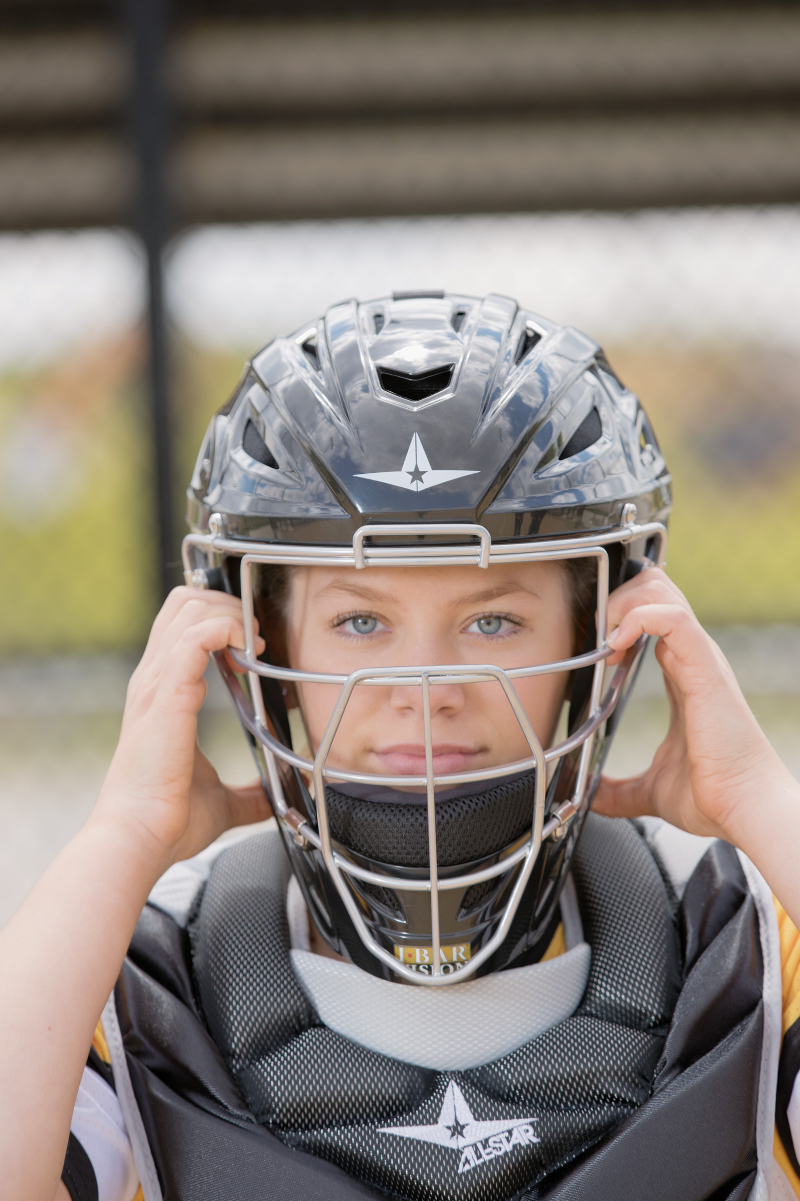 Senior portrait of a softball catcher adjusting her helmet, captured at home plate with focused expression and crisp detail during her Mueller Photography session.