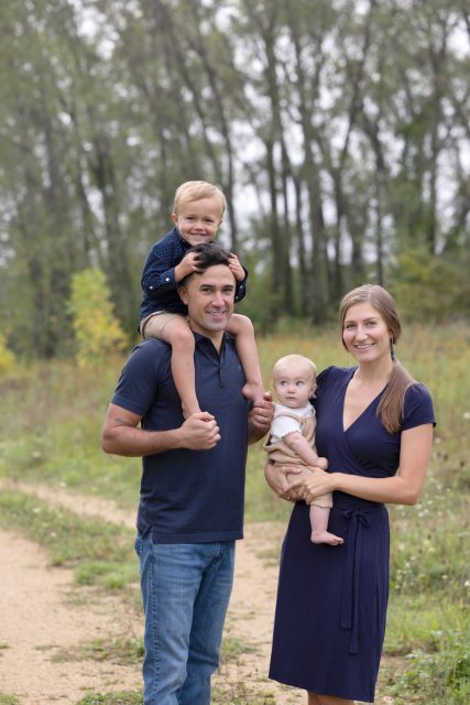 Parents with their young children outdoors, with one child sitting on their father's shoulders.