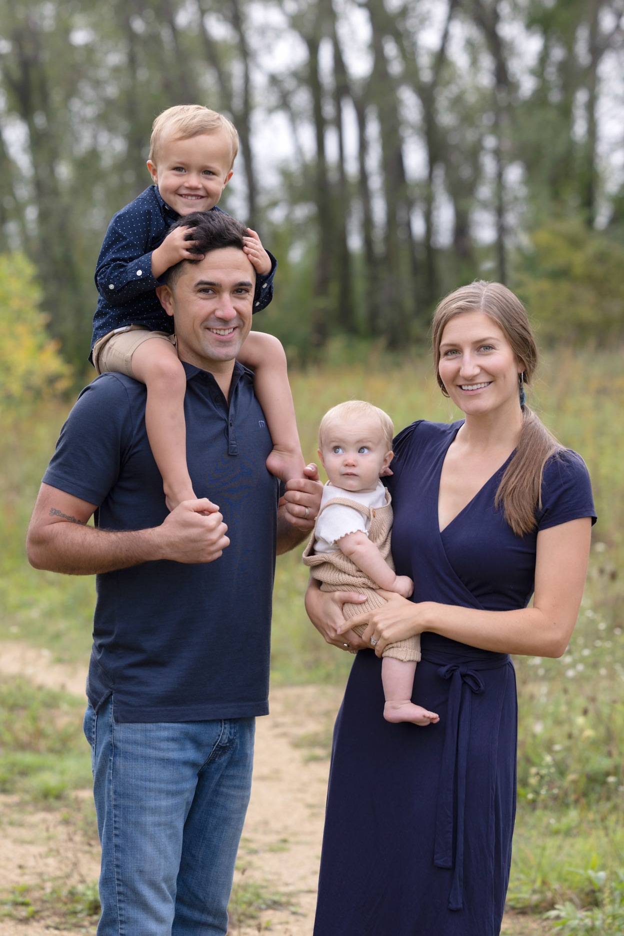 Parents with their two young children posing together outdoors during a family portrait session.