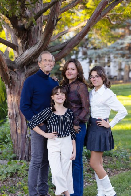 Family standing together outdoors beneath a tree during a portrait session.