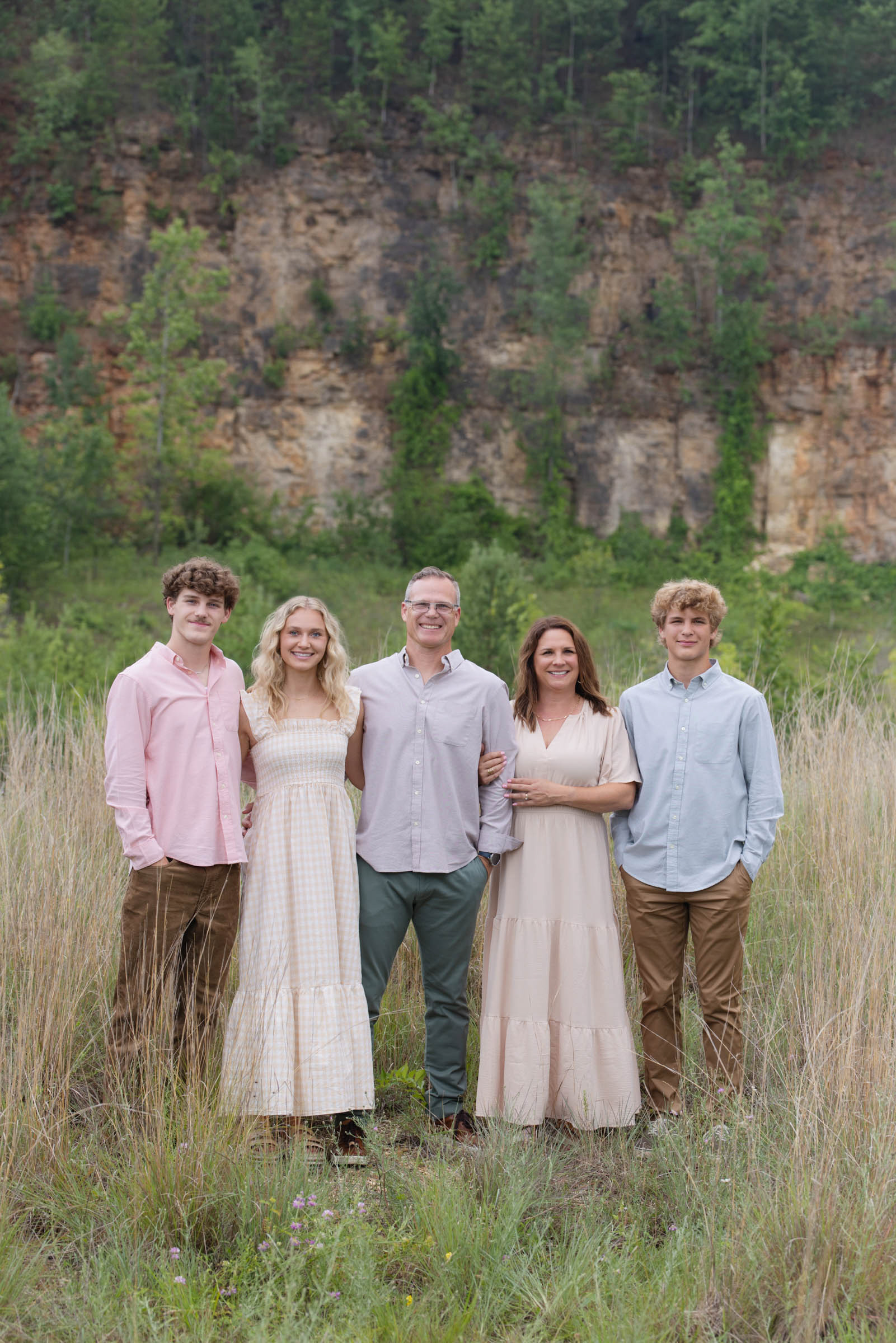Family of five standing together outdoors in tall grass during a portrait session.