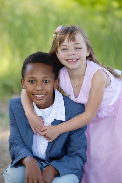 Two children smiling together during an outdoor portrait family session.