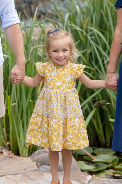 Young child holding hands with both parents while walking through tall grass.