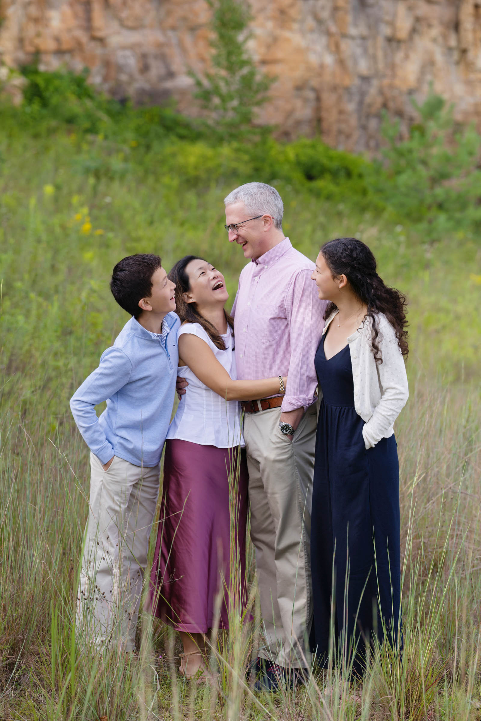 Family of four laughing together during an outdoor portrait session in a grassy field.