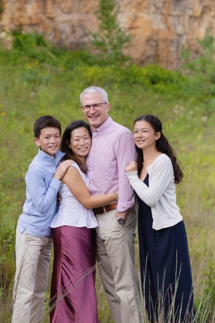 Family of four posing together outdoors in tall grass during a portrait session.