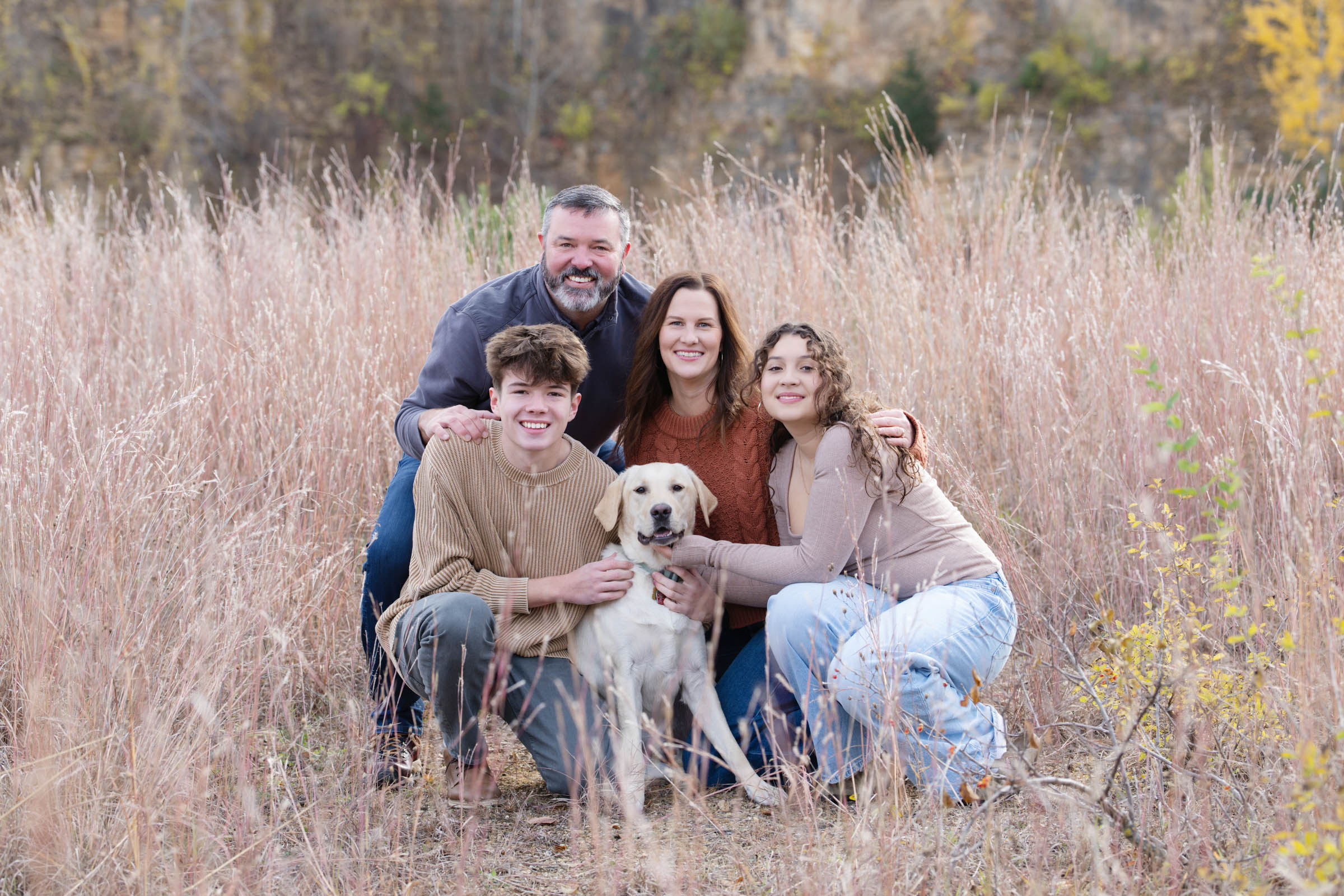 Family of four sitting together with their dog during an outdoor portrait session.