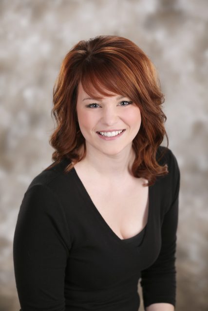 Professional business headshot of a woman smiling toward the camera against a soft neutral background.
