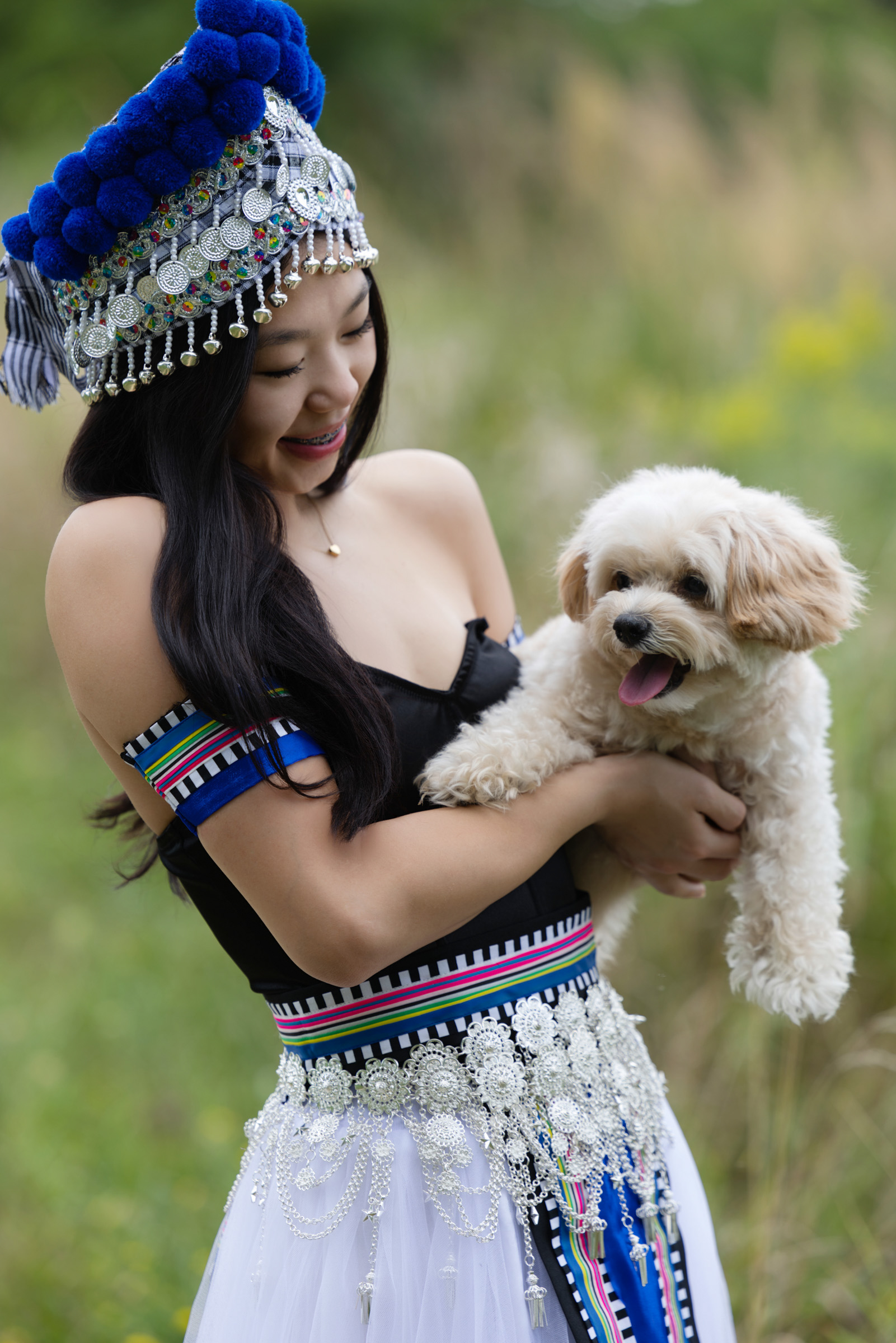 High school senior wearing cultural attire while holding her dog during an outdoor senior portrait session.