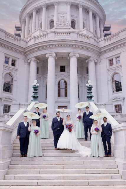 Bride, groom, and wedding party standing on the steps outside a historic government building.