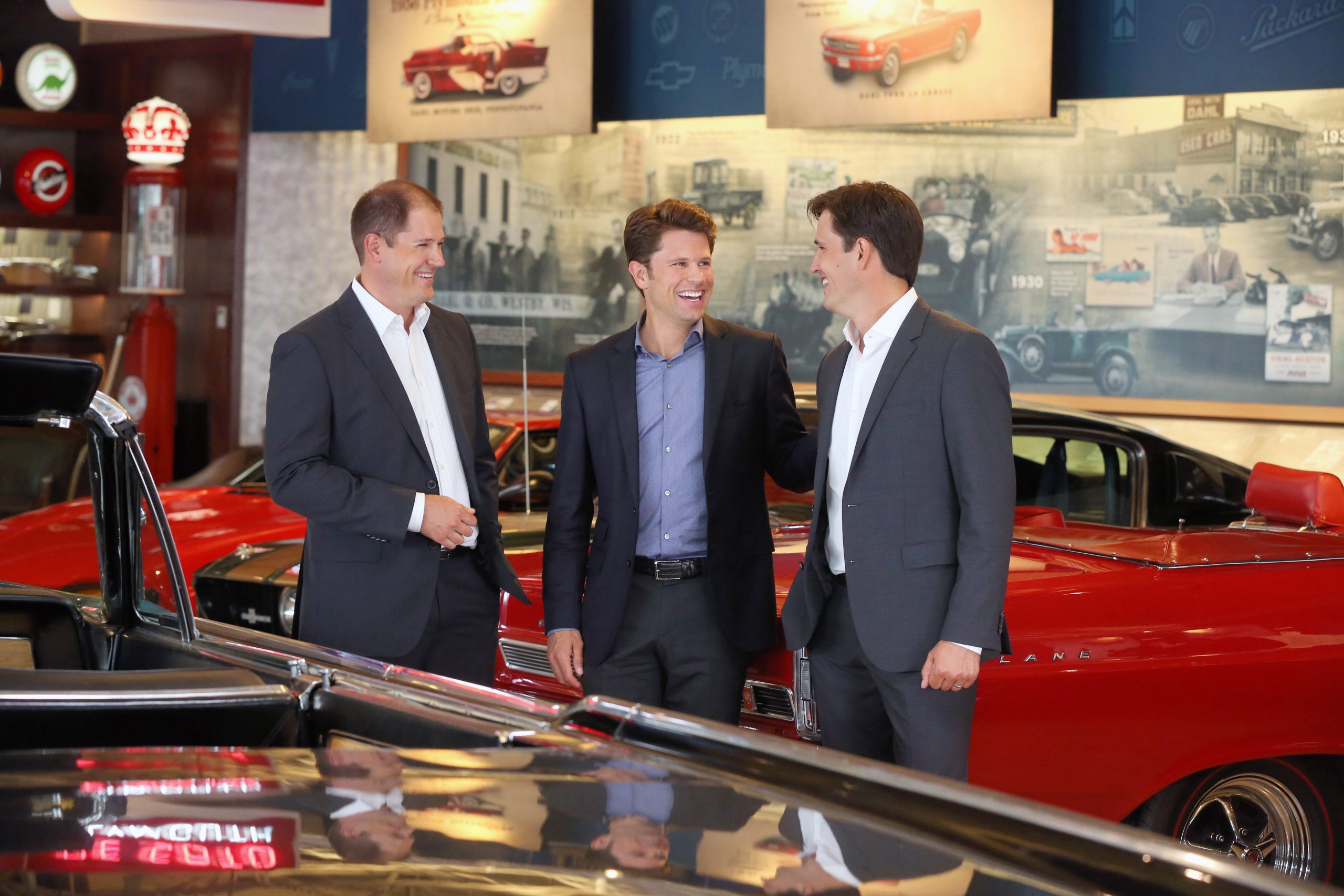 Three business professionals talking together inside a classic automobile showroom.