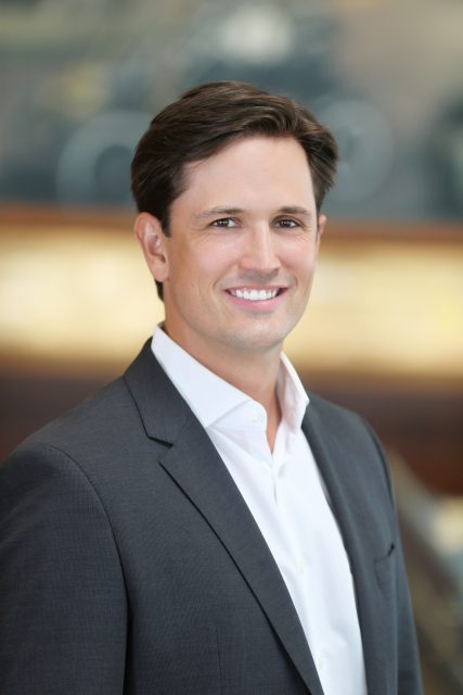 Professional headshot of a man in a suit smiling toward the camera.