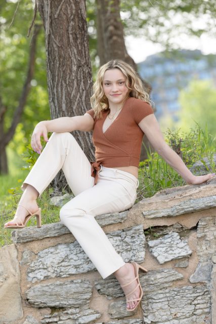 High school senior sitting on a stone wall during an outdoor portrait session.