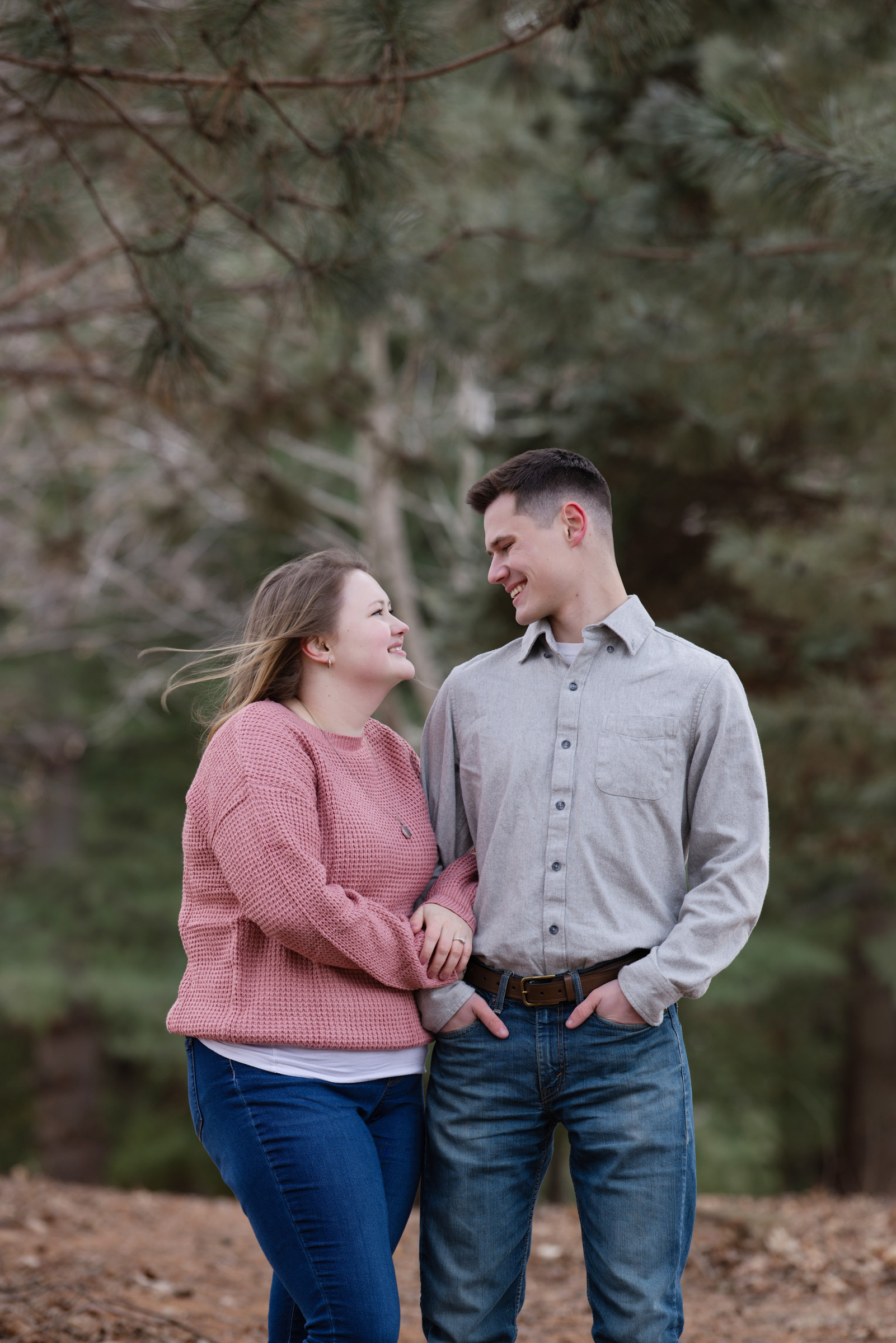 Engaged couple smiling at each other during an outdoor engagement session.
