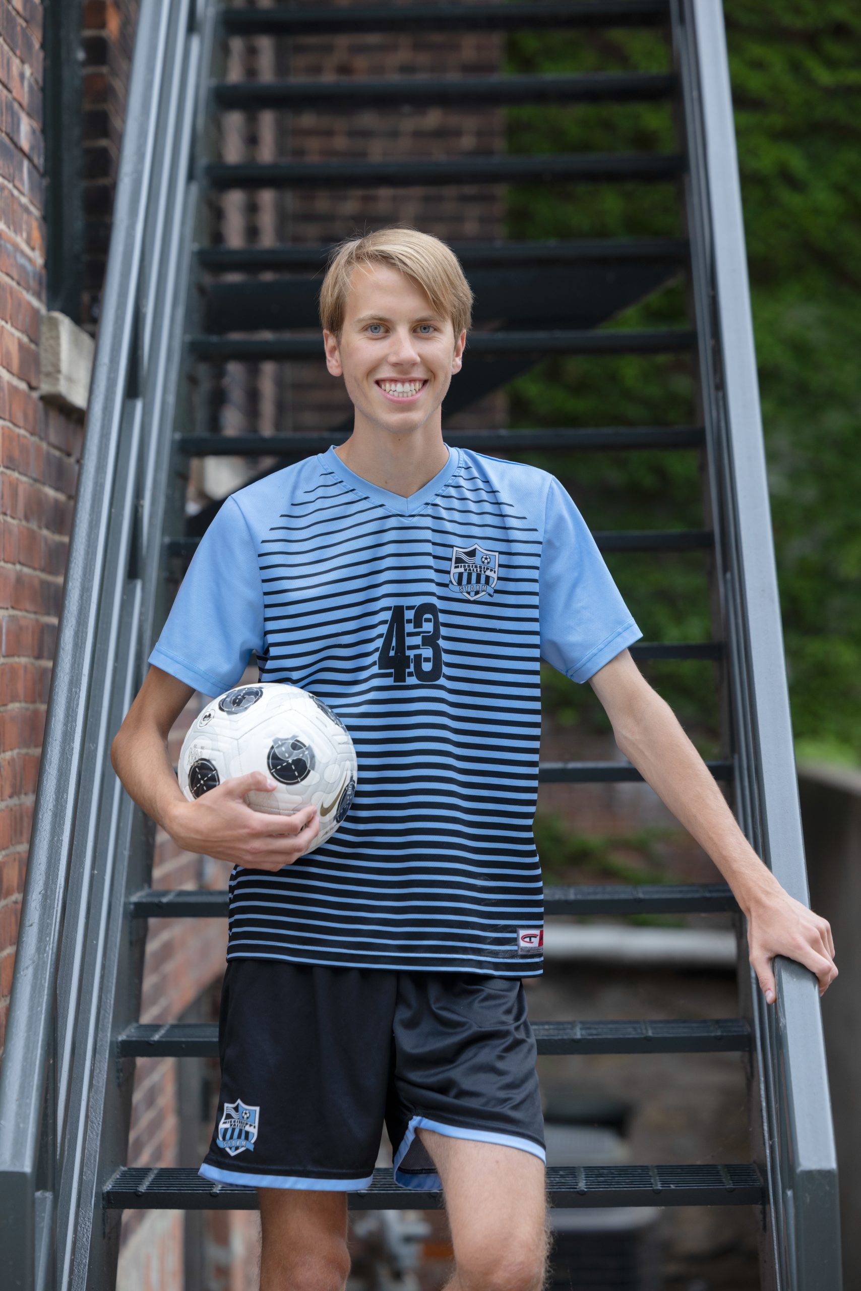 High school senior standing with a soccer ball during a portrait session.