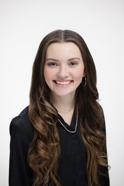 Professional headshot of a young woman smiling toward the camera against a light gray background.