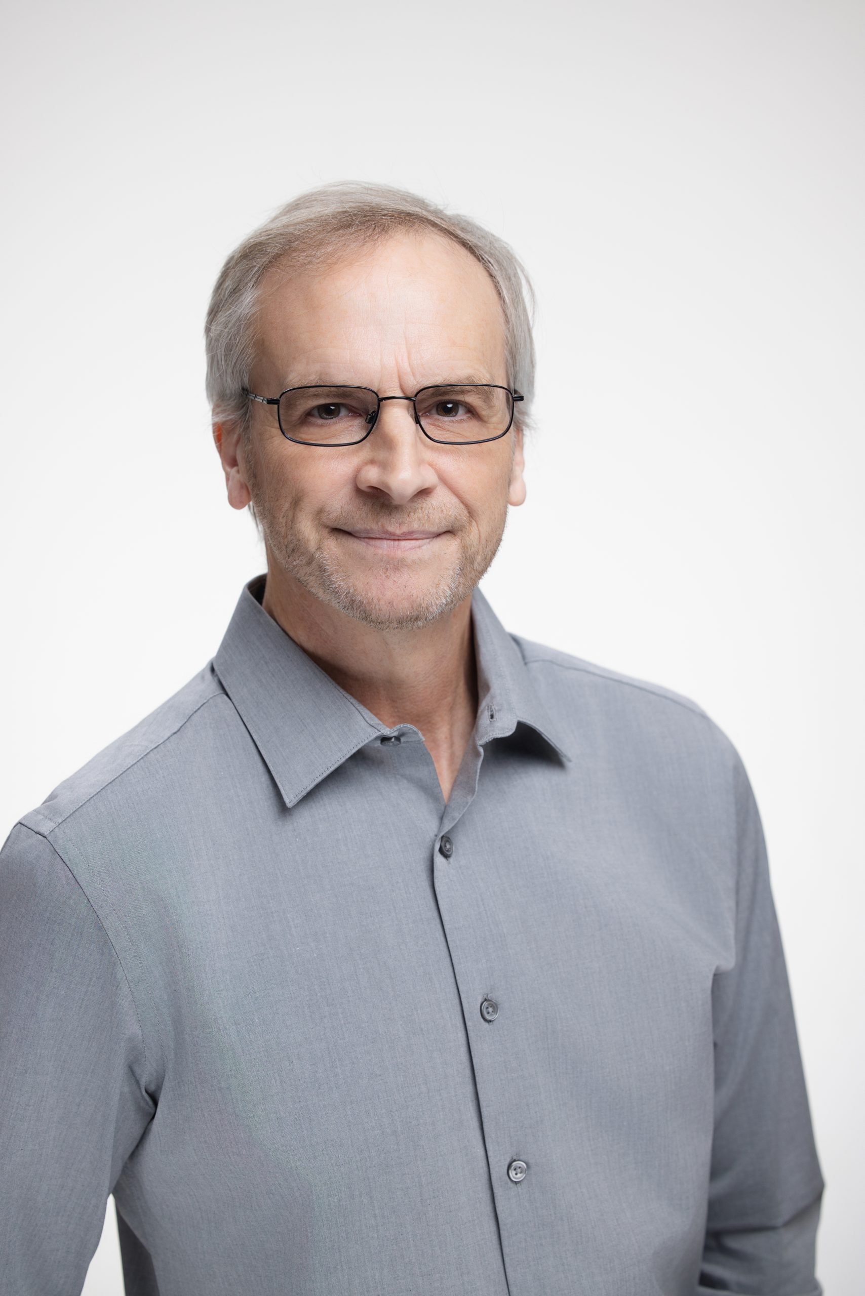 Professional headshot of a man wearing glasses and a gray button-up shirt.