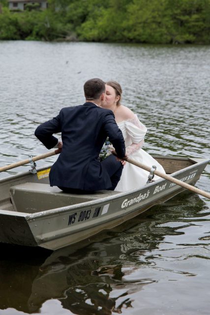 Bride and groom kissing while sitting together in a rowboat on the water.