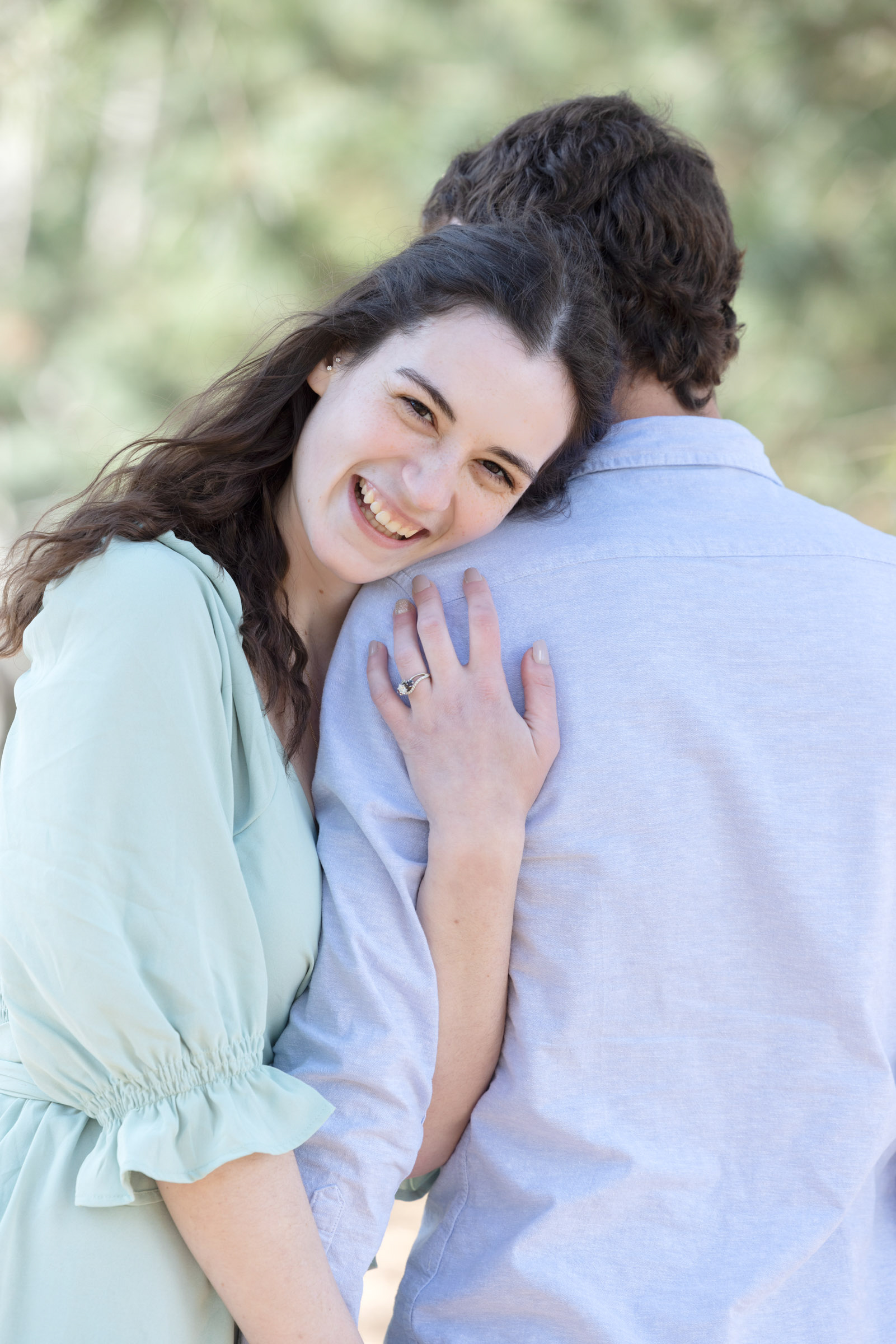 Engaged woman smiling toward the camera while standing beside her fiancé during their engagement portrait session.