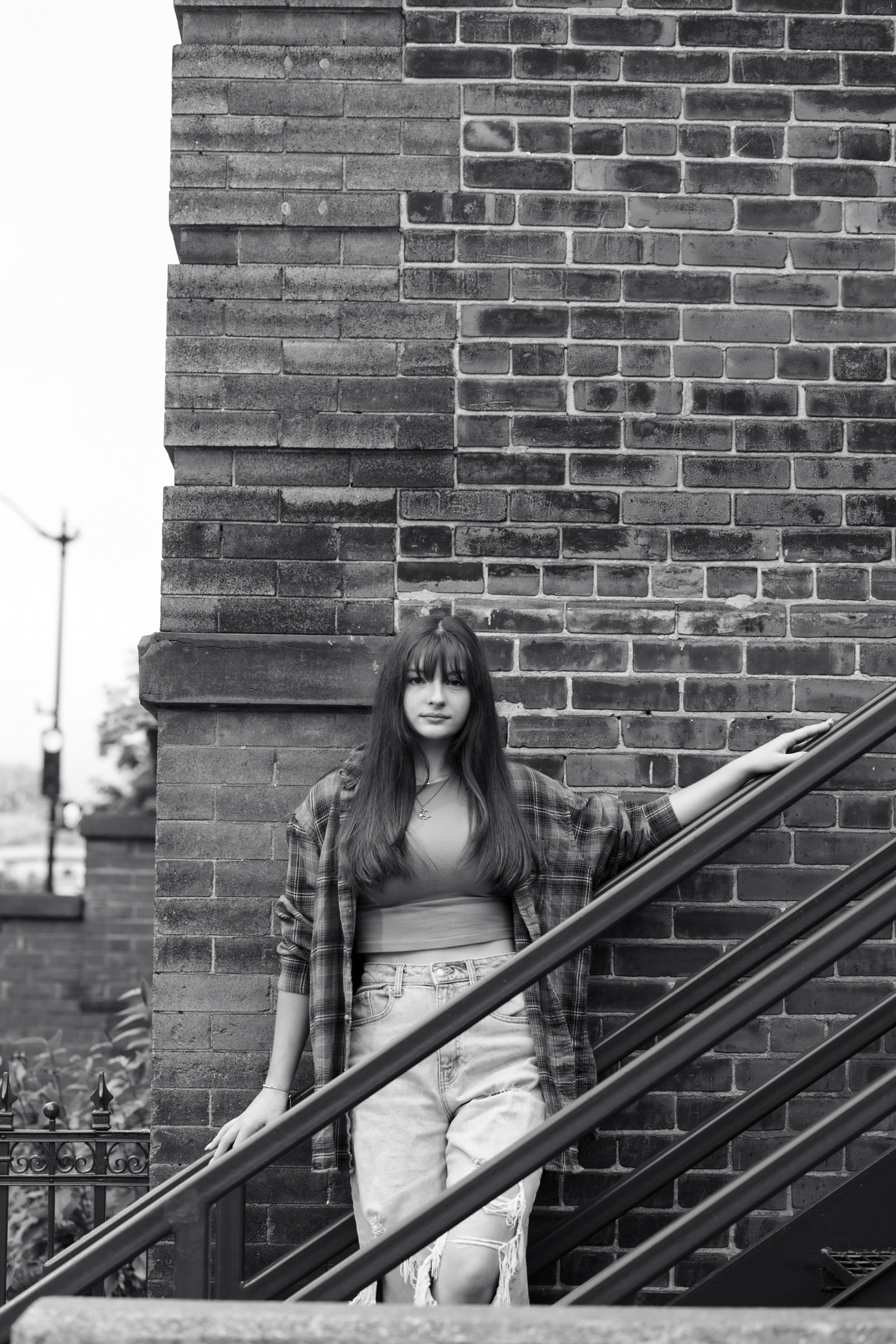 Black and white portrait of a high school senior standing near a brick wall.