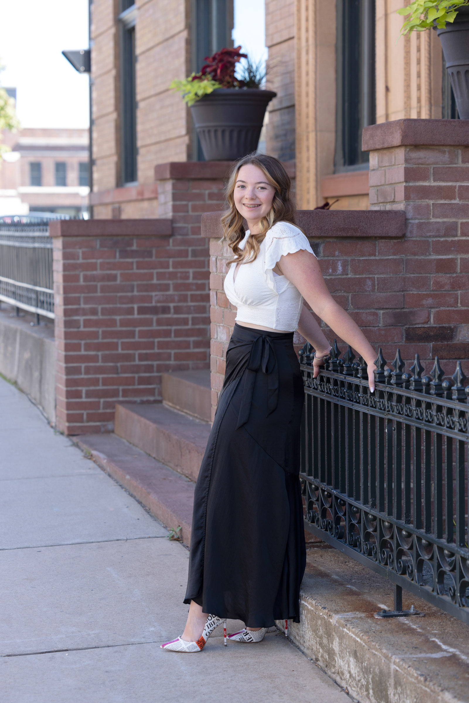 High school senior smiling while standing along a downtown sidewalk.