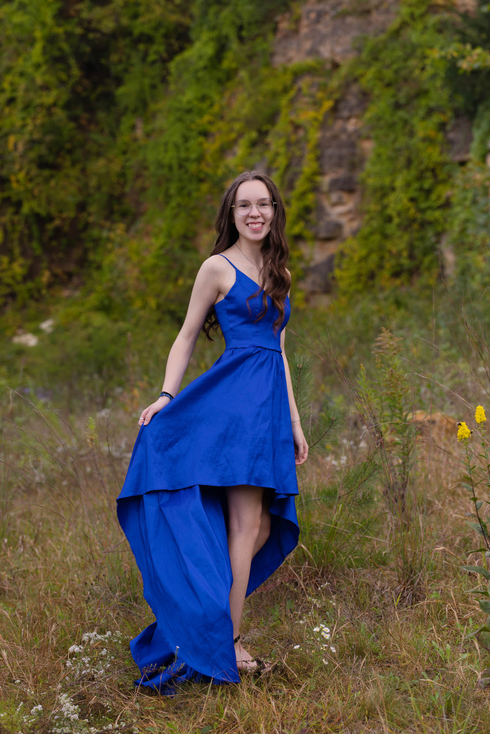 High school senior standing in a grassy field during an outdoor portrait session.