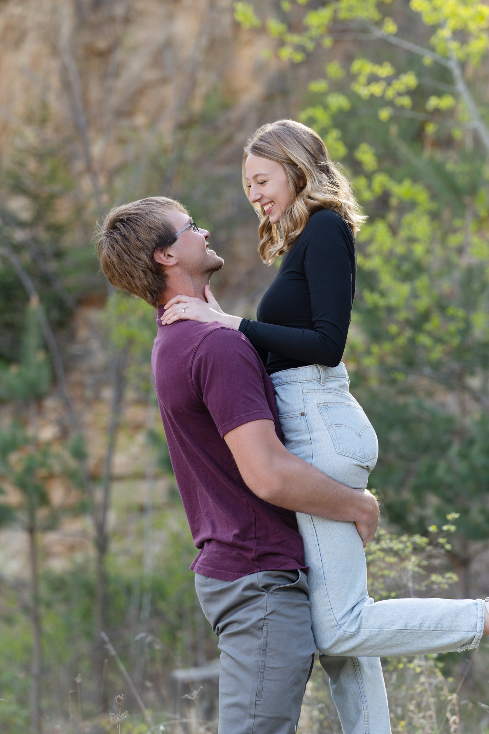 Engaged couple smiling as fiancé lifts the bride-to-be during their engagement portrait session.
