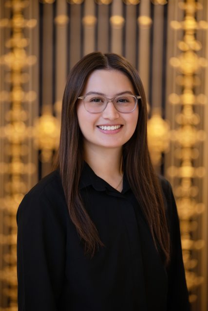 Professional headshot of a woman wearing glasses and a black shirt, smiling toward the camera indoors.