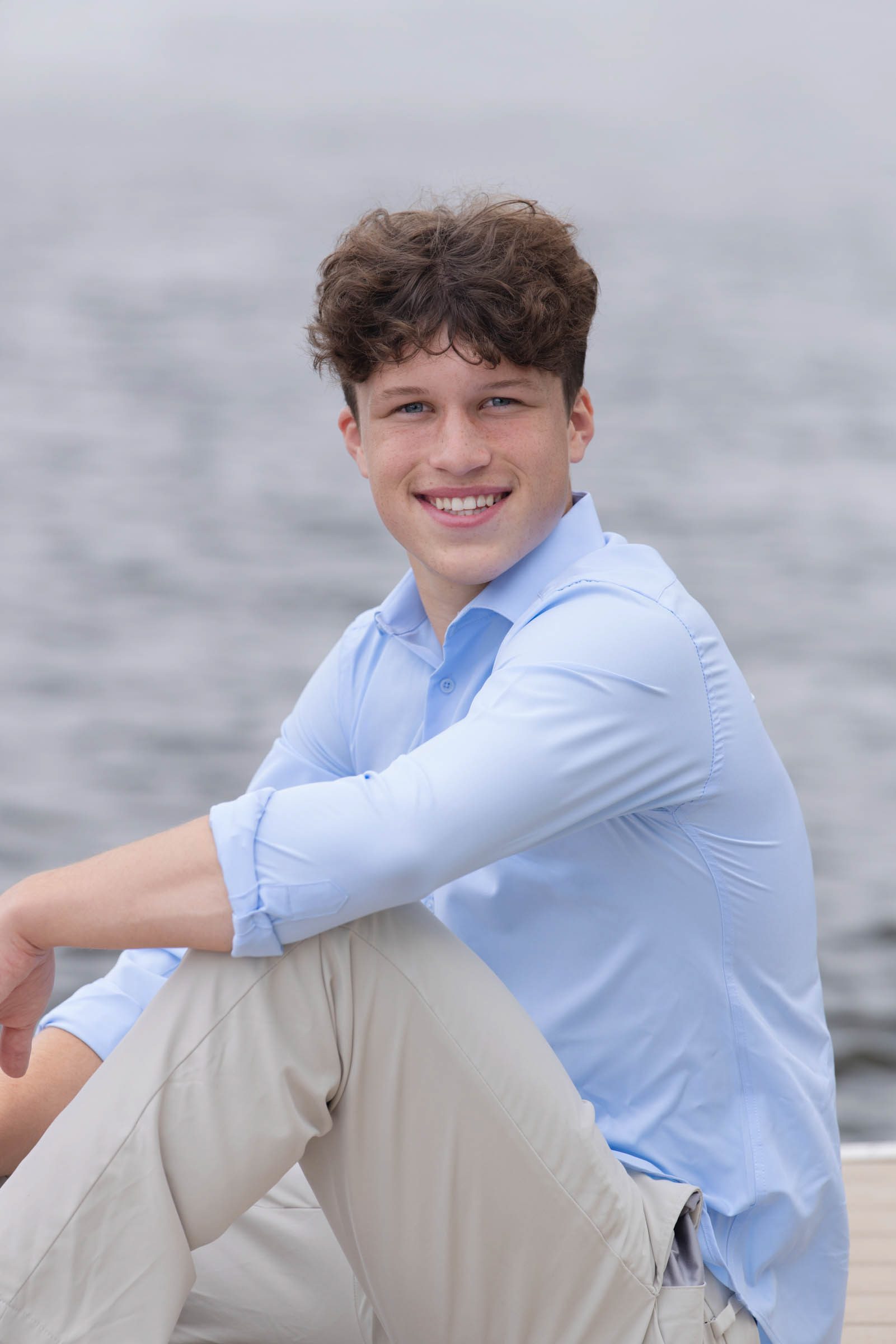 High school senior sitting outdoors and smiling during a portrait session.